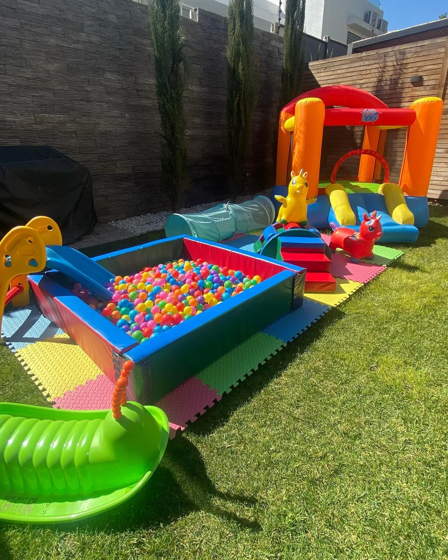 Plaza Alegría montada en un jardín: mini inflable naranjo, piscina de pelotas, túnel y módulos de espuma